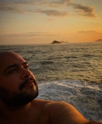 Tiago Abravanel sem camisa olhando para o horizonte com o mar de fundo