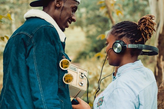 Homem e mulher negros segurando rádio e com fones de ouvido.