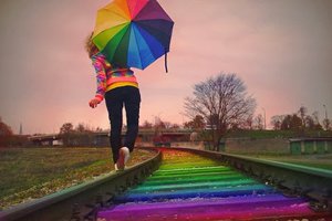 Menina andando em trilho de trem com as cores do arco-íris e segurando guarda-chuva