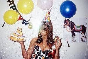 Mulher segurando bolo de aniversário, cercada opor balões e confetti.