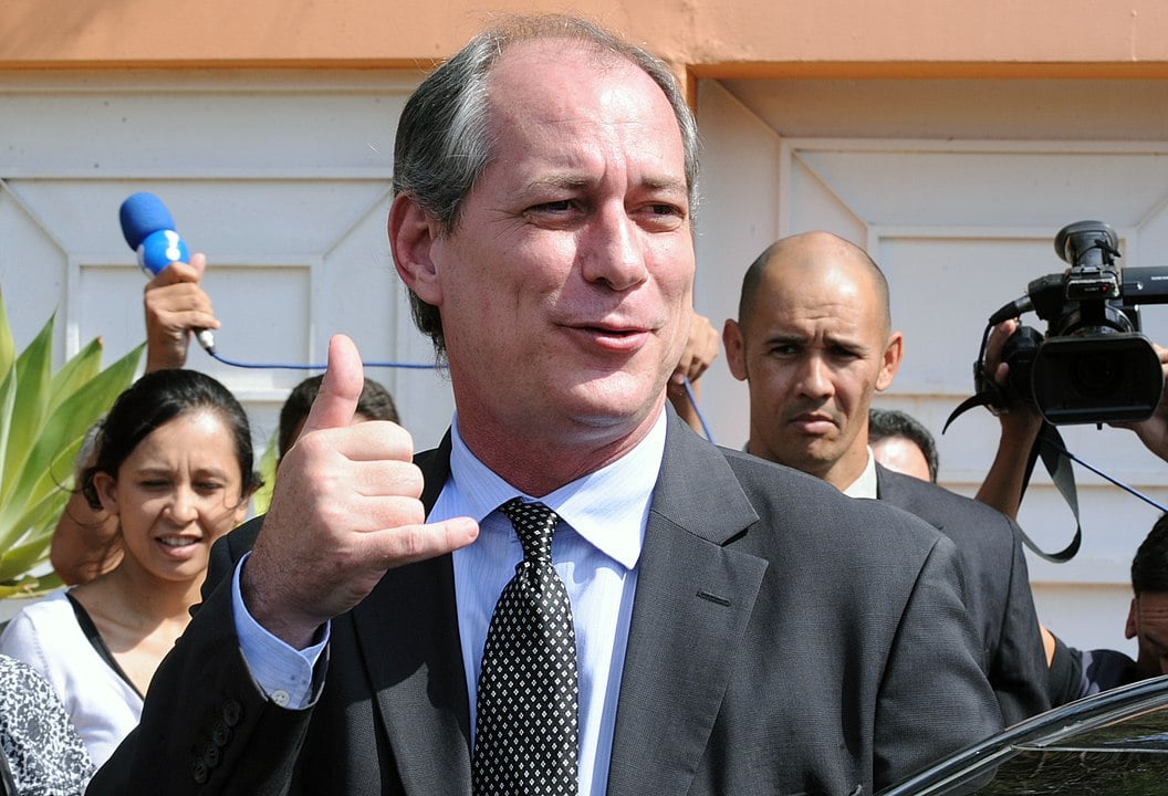 Ciro Gomes fazendo o sinal de hang loose em meio a jornalistas.