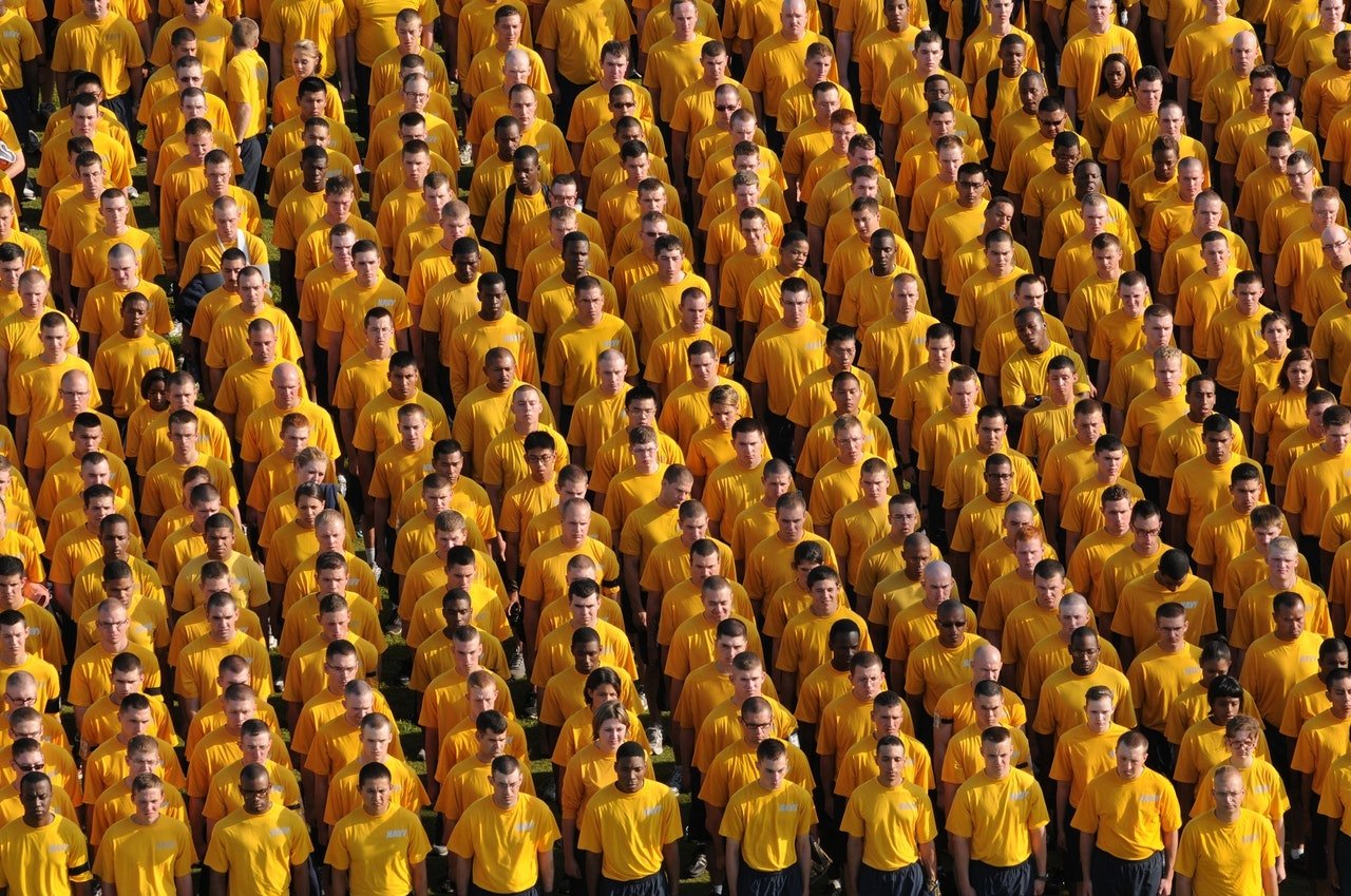 Grupo de homens em fileiras, com todos vestindo a mesma camiseta amarela lisa.