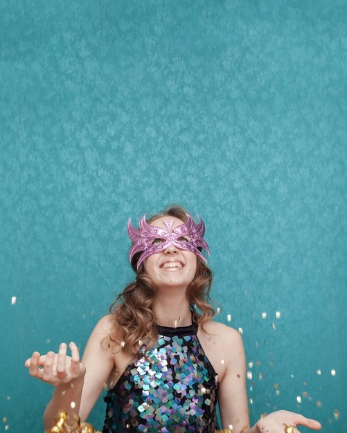 Mulher com máscara de carnaval jogando confetes para o alto.
