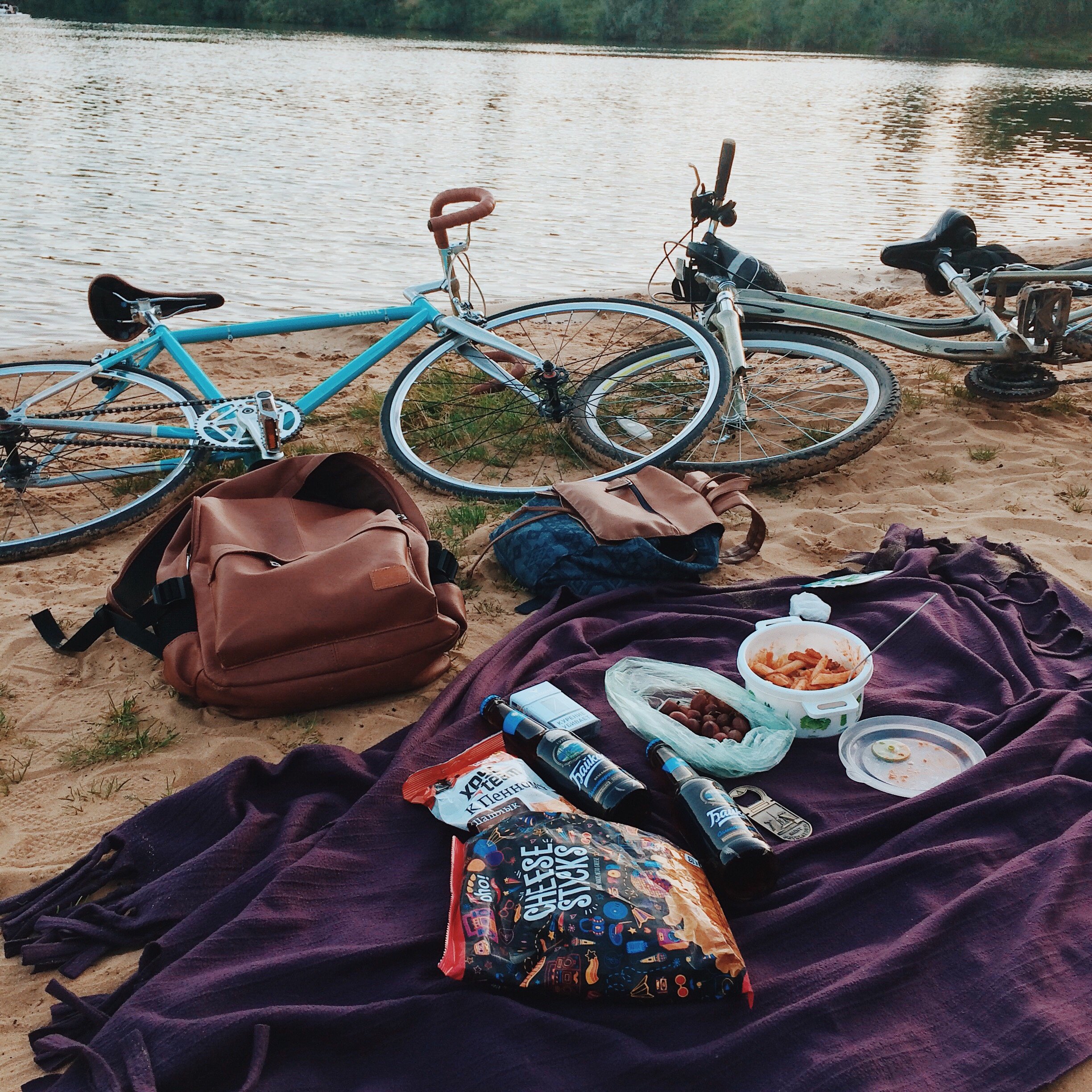 Toalha na areia com alguns alimentos e ao lado duas bicicletas de frente para o lago
