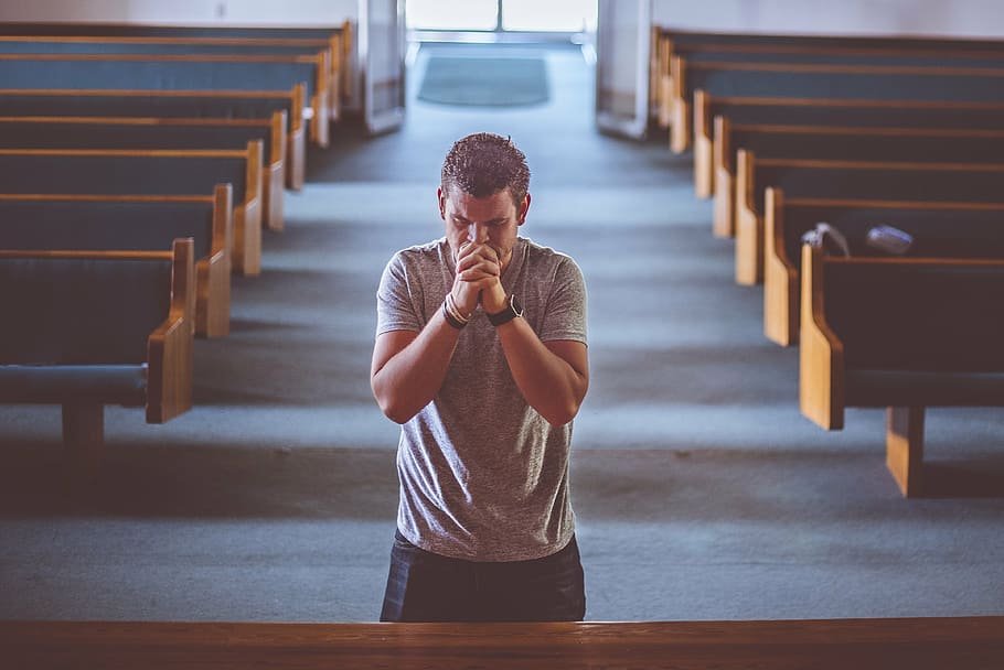 Homem com dedos entrelaçados e as mãos em frente a sua boca, rezando no altar de uma igreja.