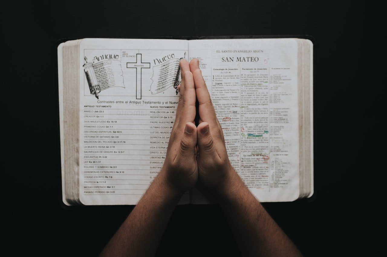 Pessoa com a palma das mãos unidas no centro de uma bíblia aberta, cheia de desenhos e anotações.