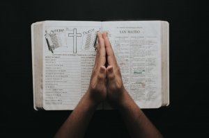 Pexels/Luis Quintero Pessoa com a palma das mãos unidas no centro de uma bíblia aberta, cheia de desenhos e anotações.