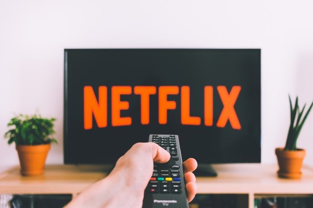 Pessoa segurando um controle remoto em frente a uma TV conectada à Netflix.