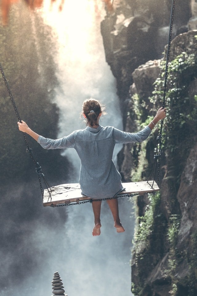 Mulher em um balanço na frente de uma cachoeira.