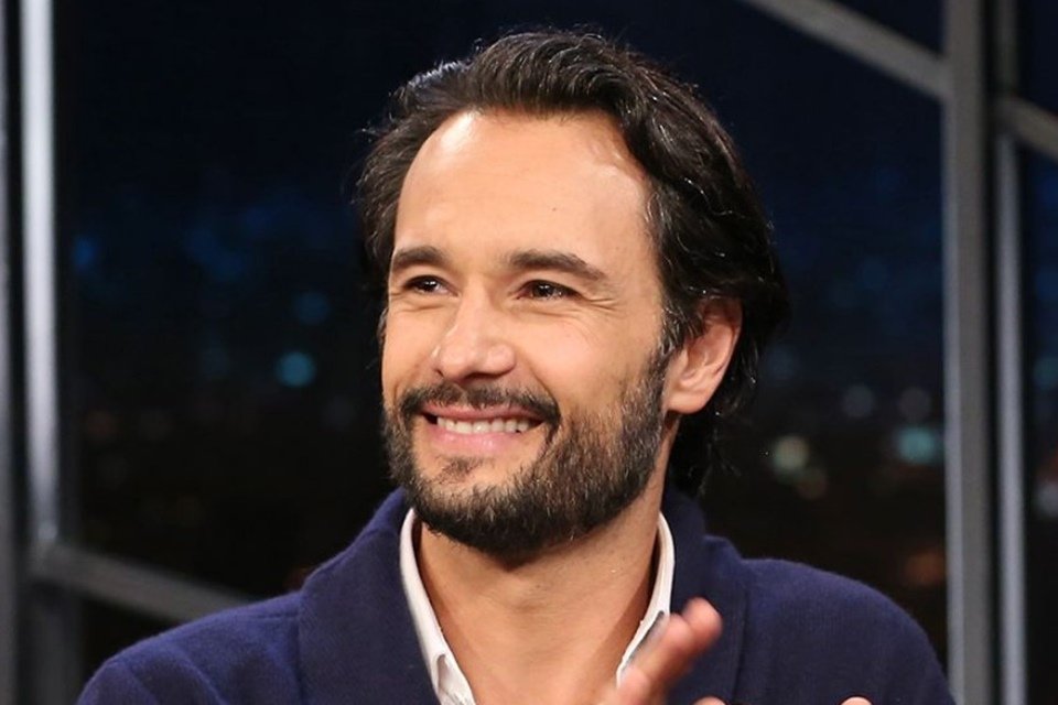 Rodrigo Santoro de lado e sorrindo durante um programa de entrevistas.