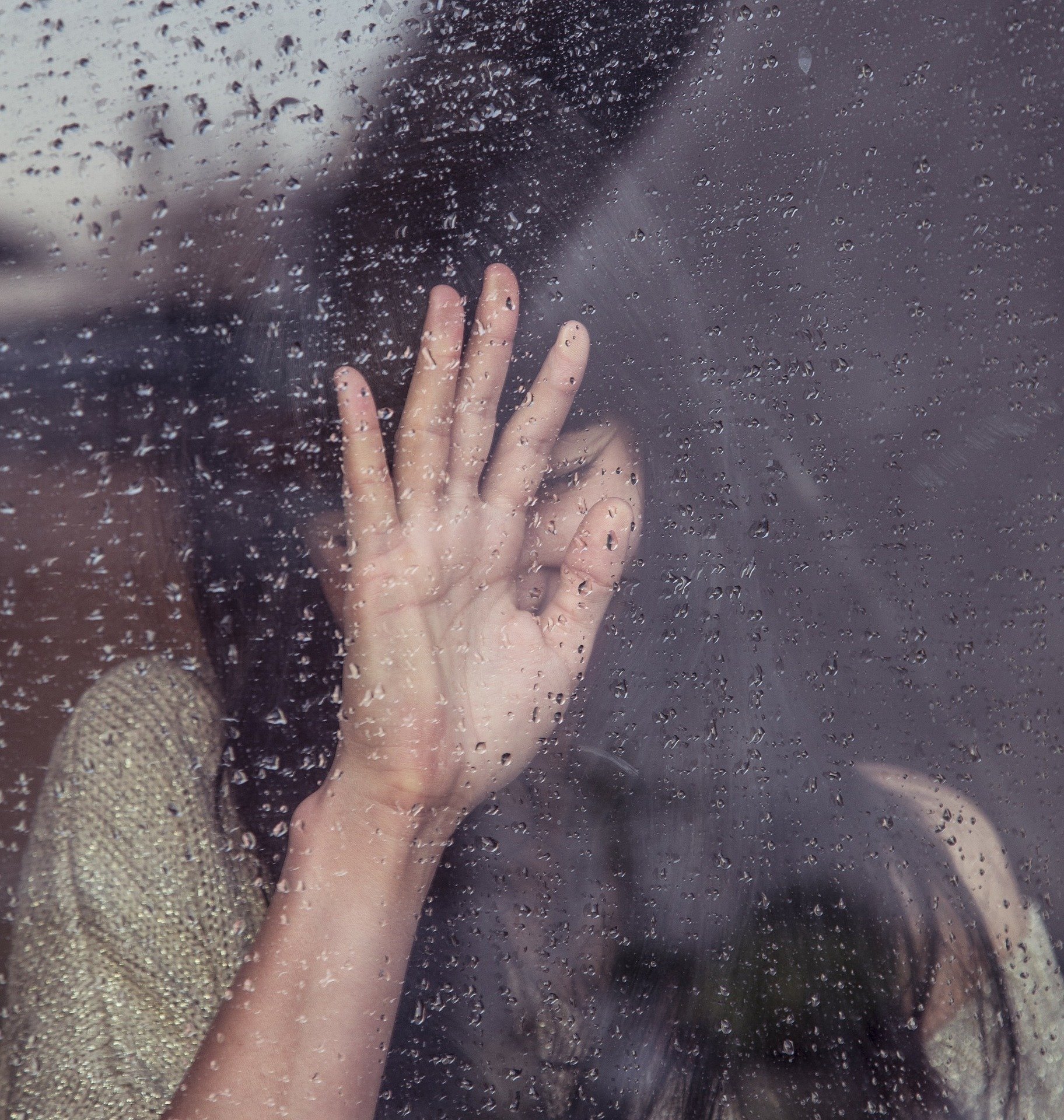 Mulher triste com a mão na janela  com gotas de chuva