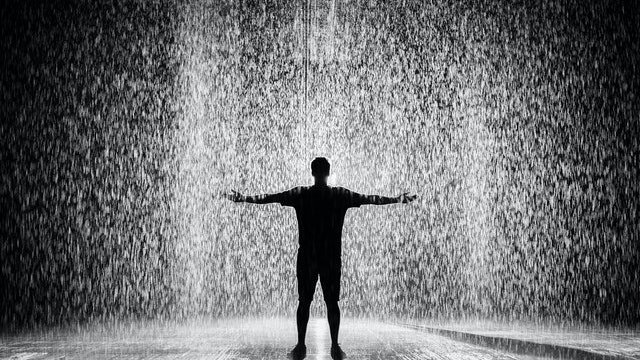 Silhueta de homem com braços abertos na chuva.