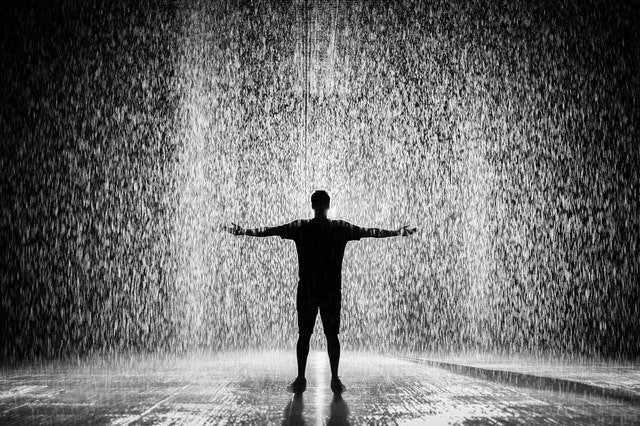 Silhueta de homem com braços abertos na chuva.