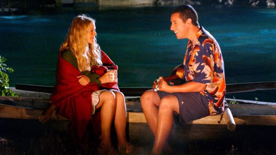 Adam Sandler e Drew Barrymore como seus personagens Henry e Lucie sentados na beira da água enquanto ele toca uma música para ela