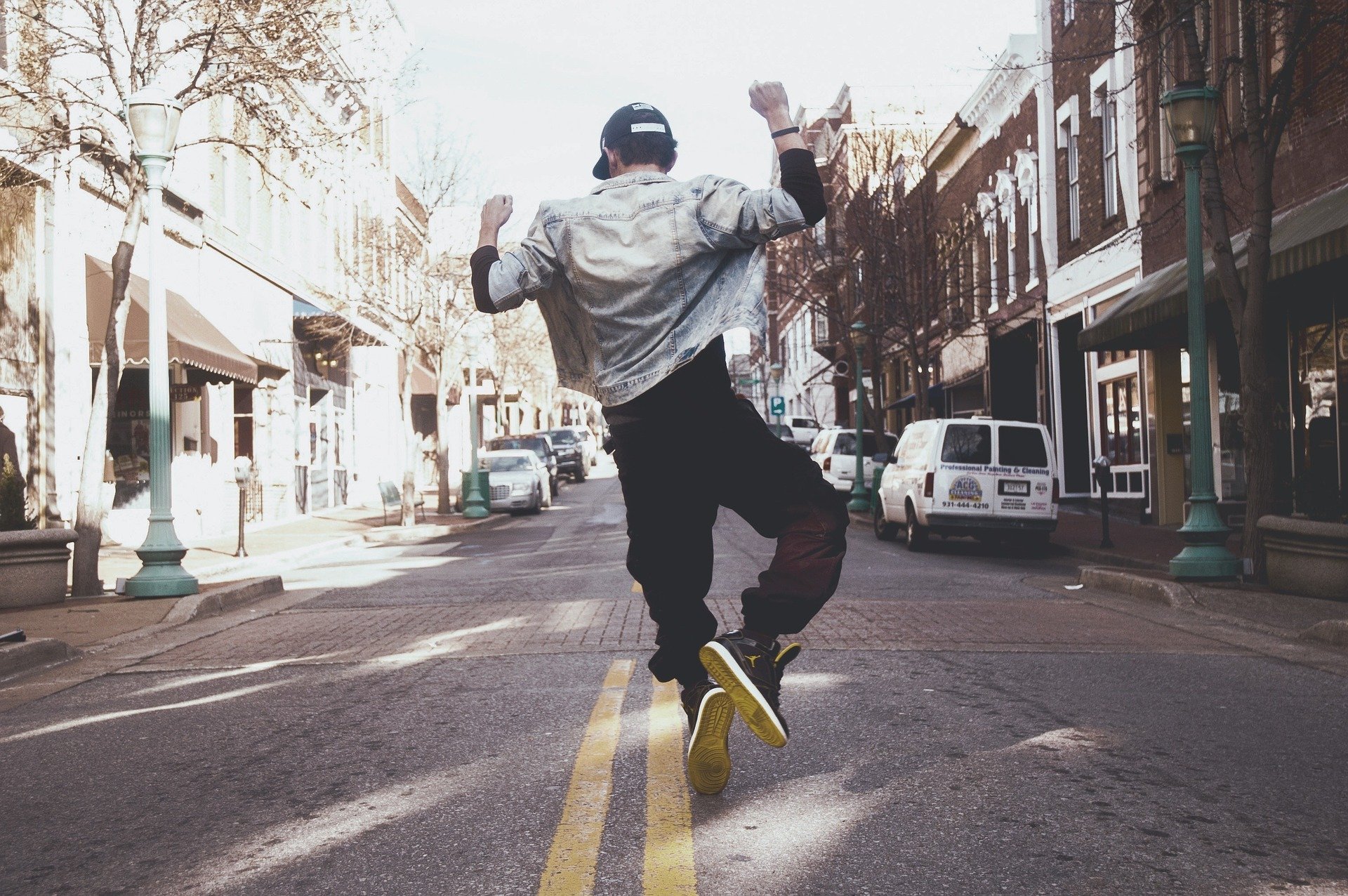 Homem pulando no meio da rua usando jaqueta e boné