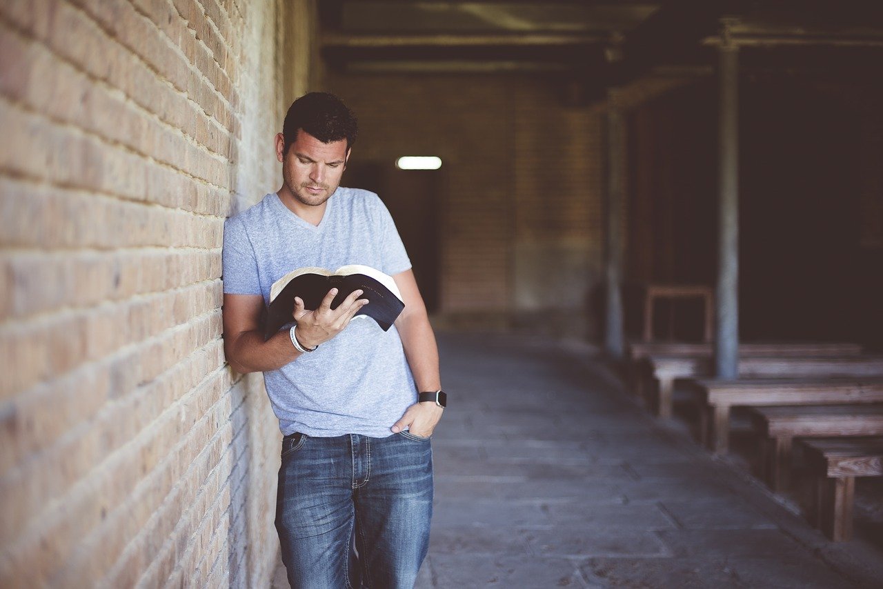 Homem lendo bíblia ao lado da parede a igreja