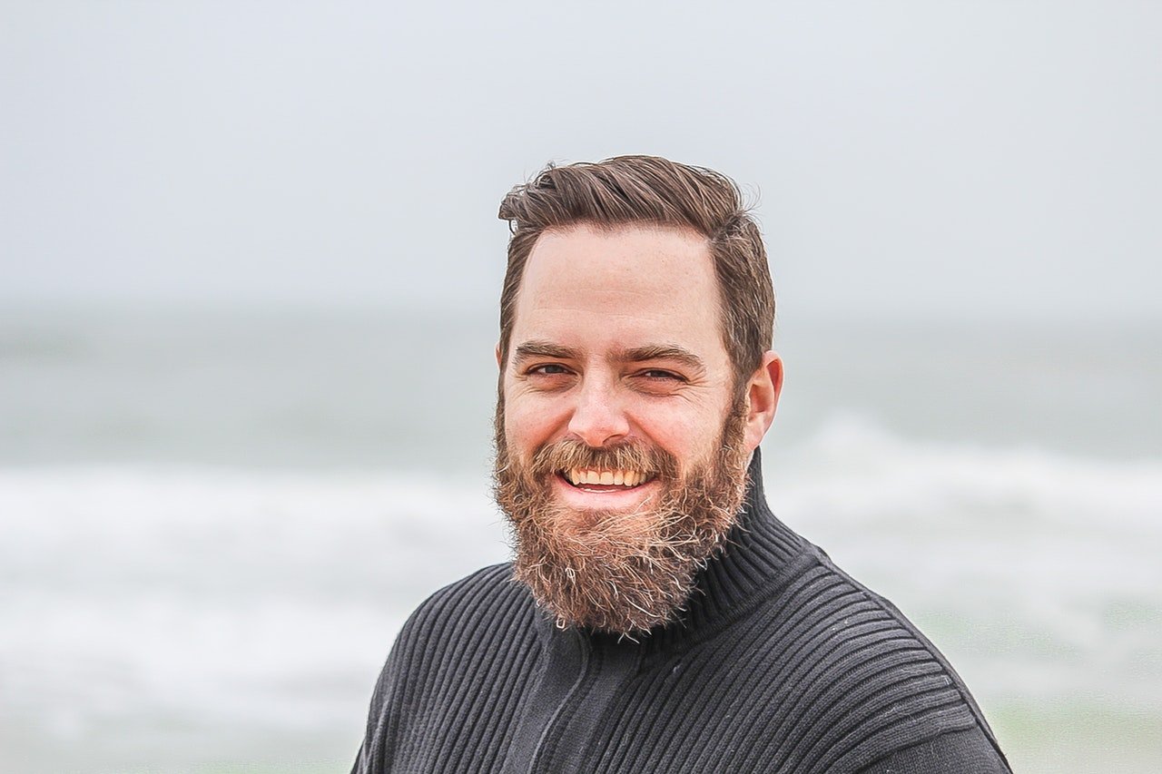 Homem de barba feliz com mar ao fundo