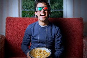 Homem com óculos 3D segurando balde de pipoca ao assistir a um filme.