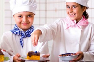 Duas crianças com roupas de chef fazendo um bolo.