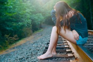 Garota triste sentada em trilho de trem com mão apoiada no joelho e na cabeça
