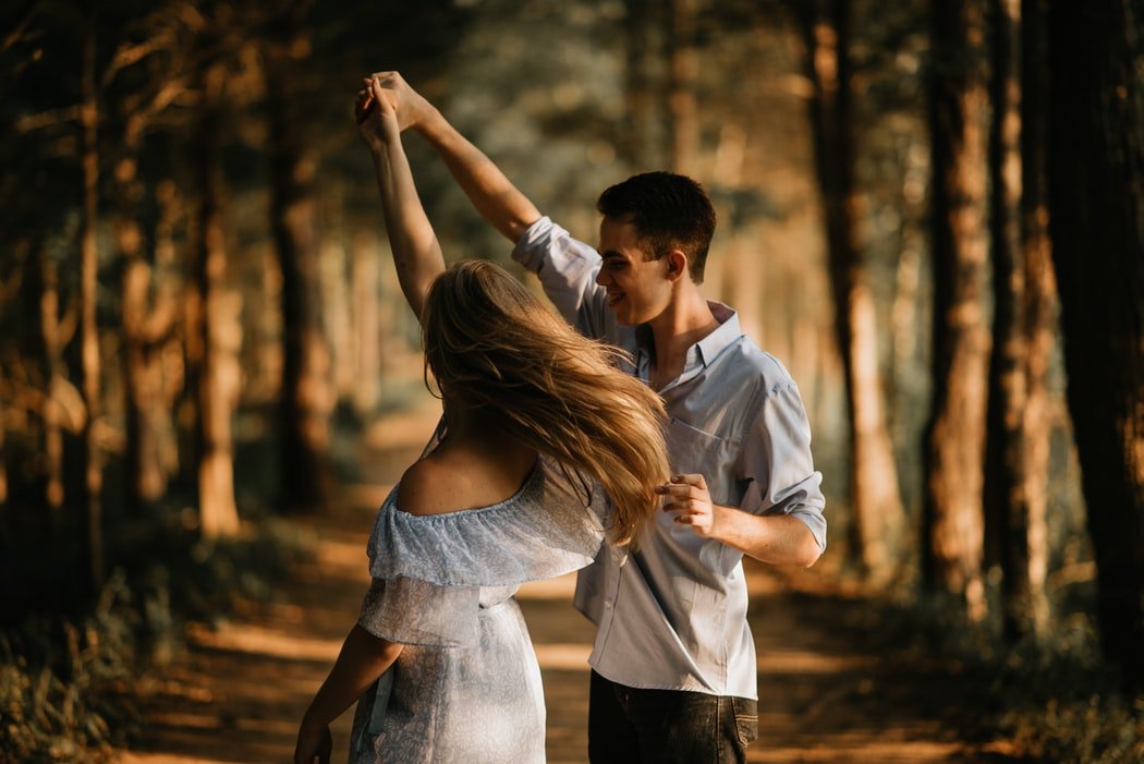 Casal dançando entre árvores. O homem está girando a mulher.