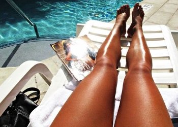 Mulher bronzeada tomando sol do lado de uma piscina.