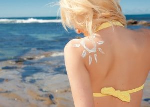 Mulher com protetor solar nas costas em frente à praia.
