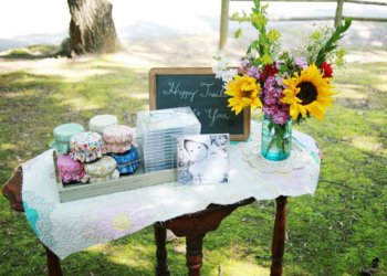 Mesa com arranjo de flores, lousa, fotos e potes enfeitados do lado de fora em gramado