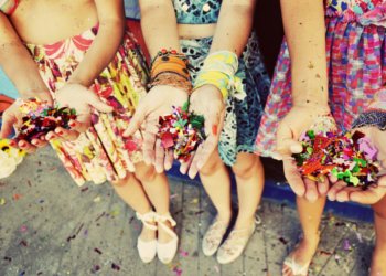 Mãos com confetes coloridos e fantasias de carnaval vistas de cima