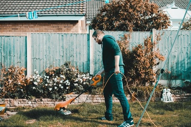 Homem cortando grama com aparador elétrico em um jardim.