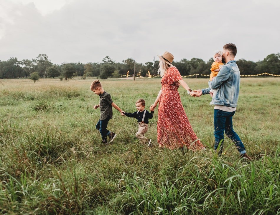 Família de homem, mulher e três filhos crianças andando em um campo, de mãos dadas.