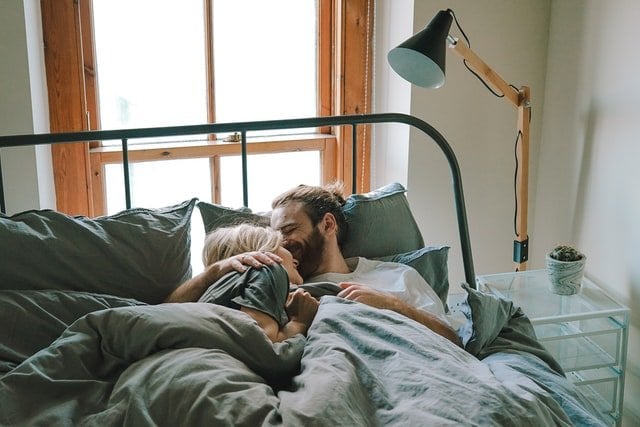 Homem e mulher deitados na cama, abraçados e sorrindo
