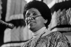 Audre Lorde falando no microfone e sorrindo