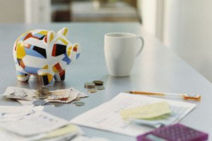 Cofre de porco, dinheiro, papéis, calculadora e xícara em cima de uma mesa