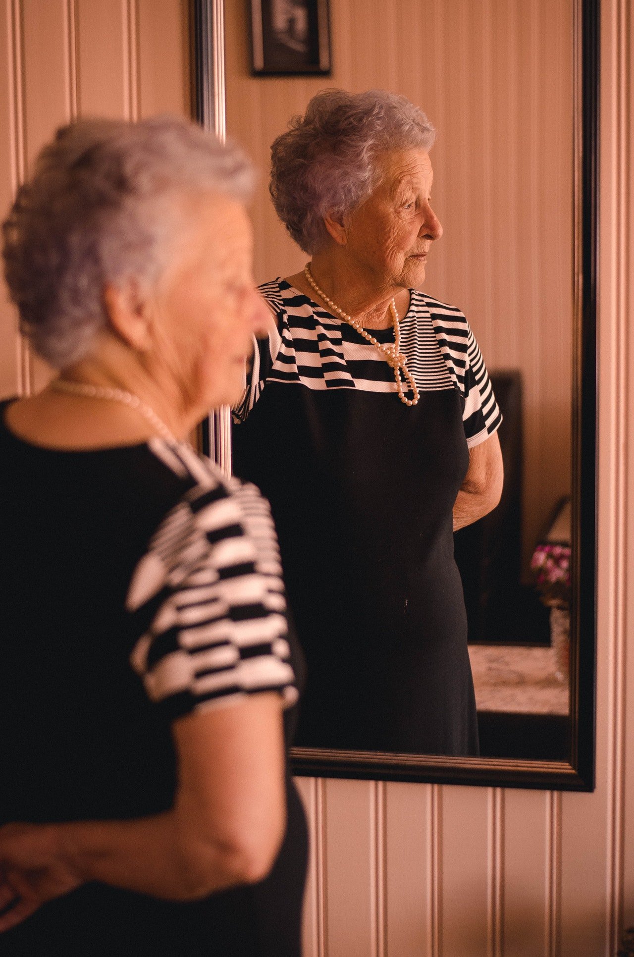 Mulher idosa na frente de um espelho, olhando para o lado