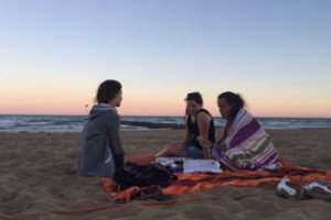Três amigas sentadas na areia da praia.