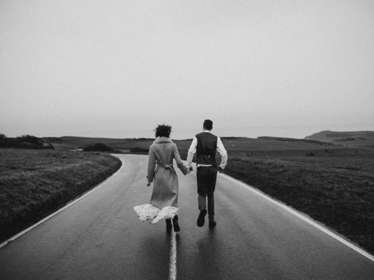 Homem e mulher correndo de mãos dadas em uma estrada molhada.