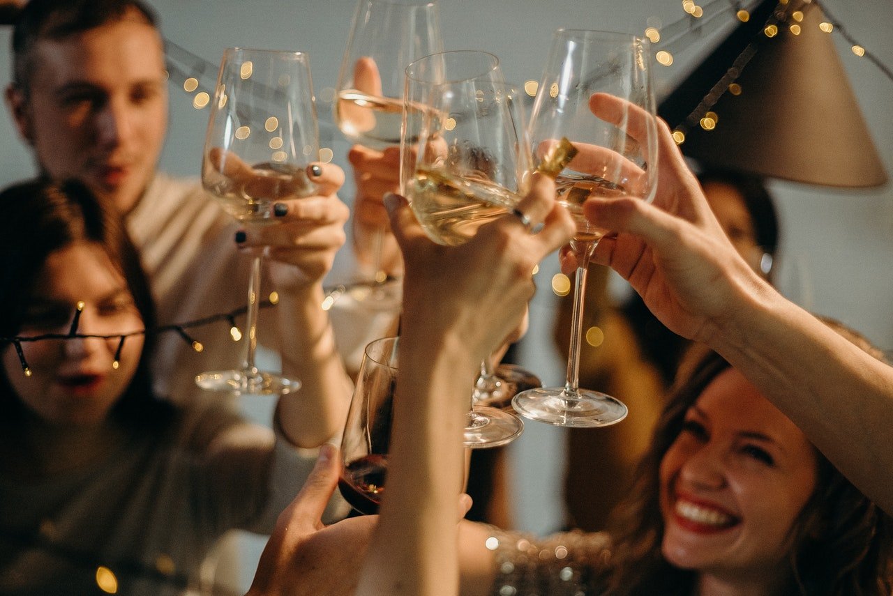 Pessoas brindando com taças contendo vinho branco.