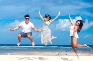 Pexels - Artem Beliaikin Três pessoas pulando enquanto sorriem em uma praia num dia ensolarado.