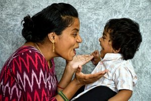 Foto de família com pai segurando bebê com mãe ao lado e filho maior em pé em frente ao casal
