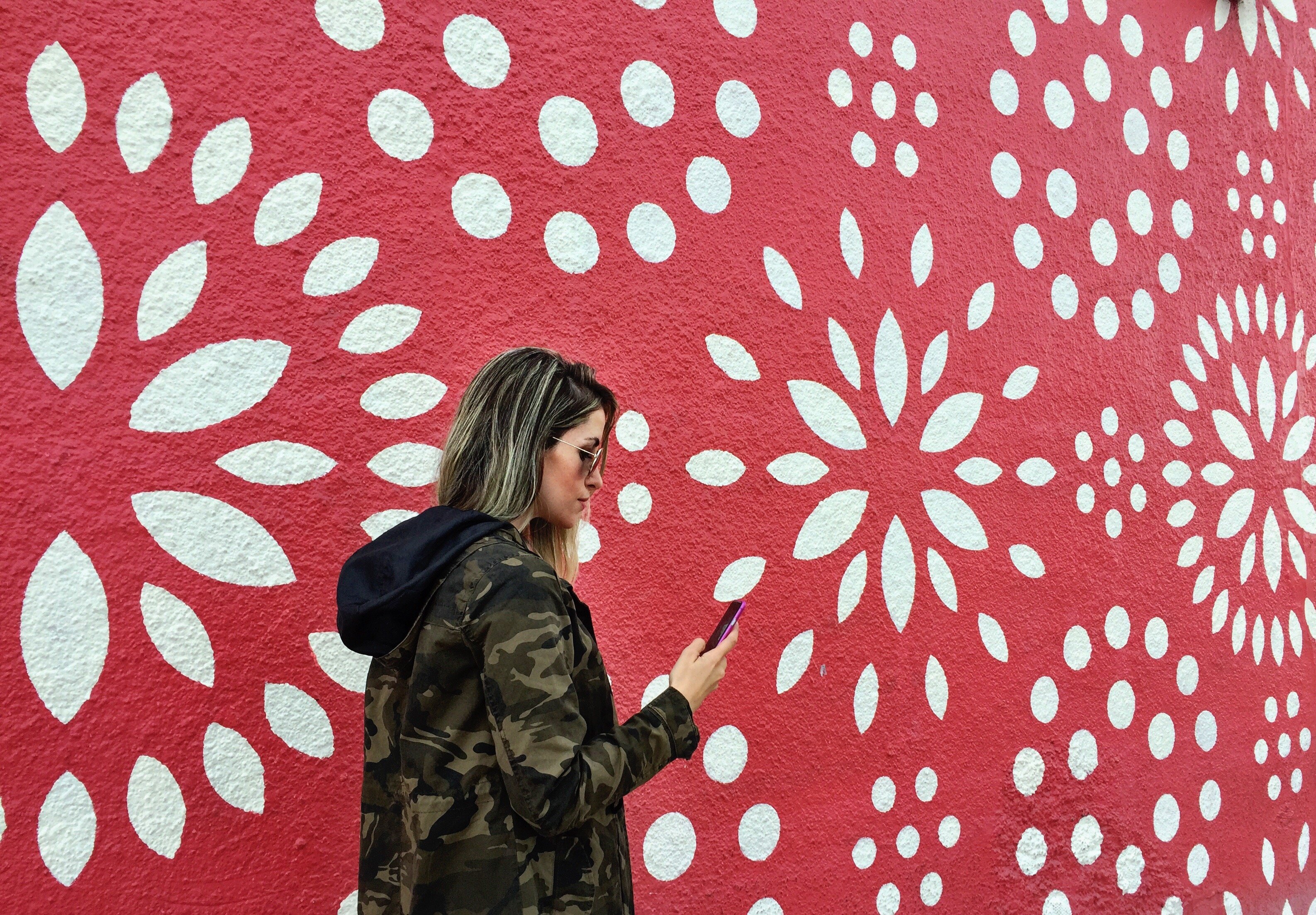 Mulher segurando celular ao lado de uma parede pintada