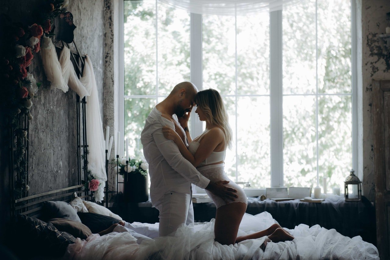 Homem e mulher abraçados de joelhos na cama.