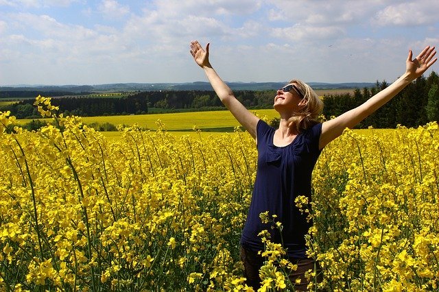 Mulher de braços abertos, sorrindo para o céu, em um campo florido.
