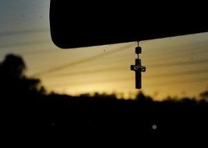 Terço pendurado em retrovisor de carro durante o nascer do sol.
