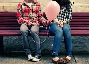 Casal sentado em banco de praça, enquanto menino entrega balão para menina