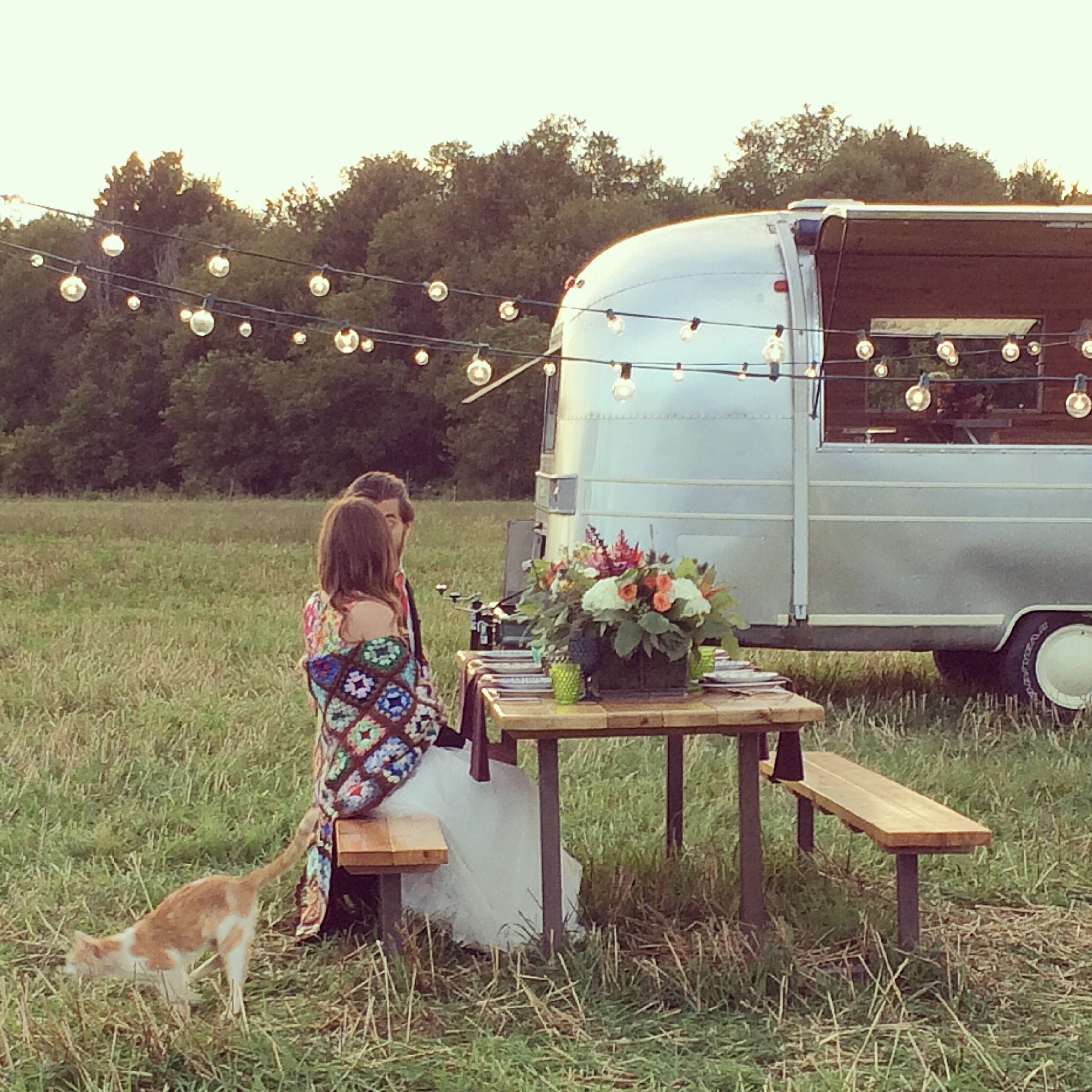 Casal em uma mesa de madeira conversando ao lado de um trailer