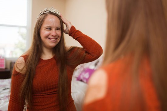 Mulher sorrindo olhando para o espelho e segurando coroa em sua cabeça