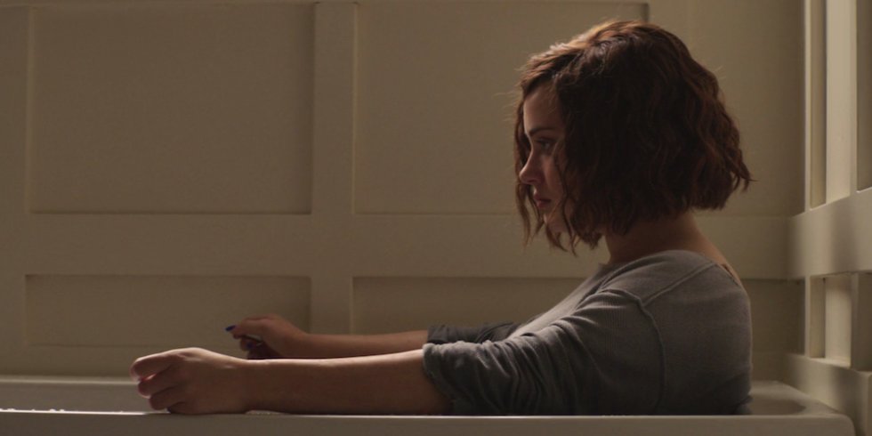 Hannah dentro da banheira usando uma blusa de manga comprida, com as mangas puxadas para deixar seus braços expostos.