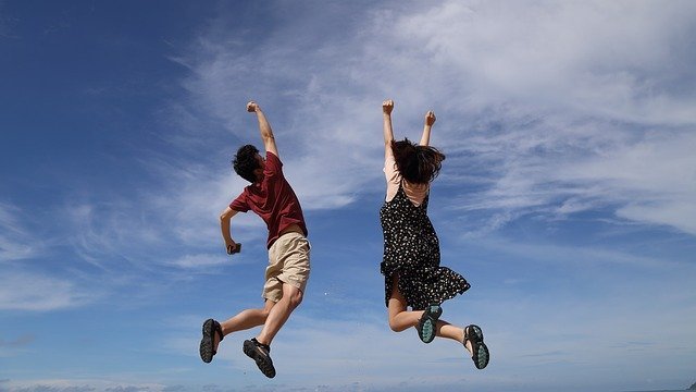 Duas pessoas pulando com os braços para o alto, com o céu azul de fundo.