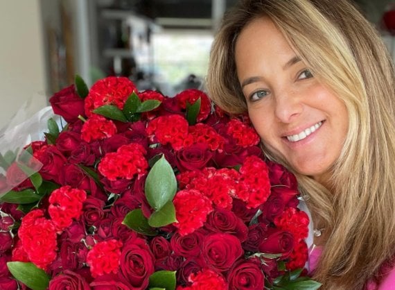 Ticiane Pinheiro segurando enorme buquê de flores vermelhas e sorrindo para selfie